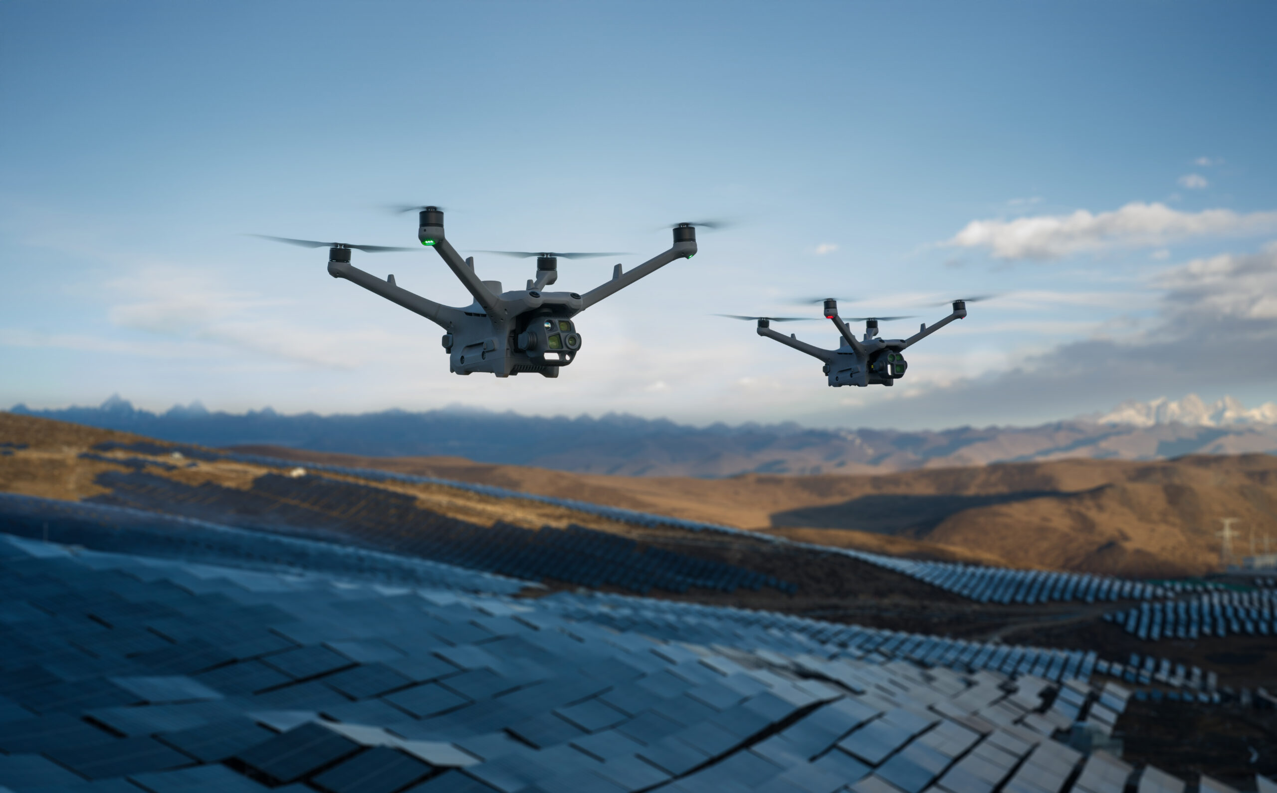 Zwei Drohnen fliegen über einem großen Solarpark in einer Berglandschaft