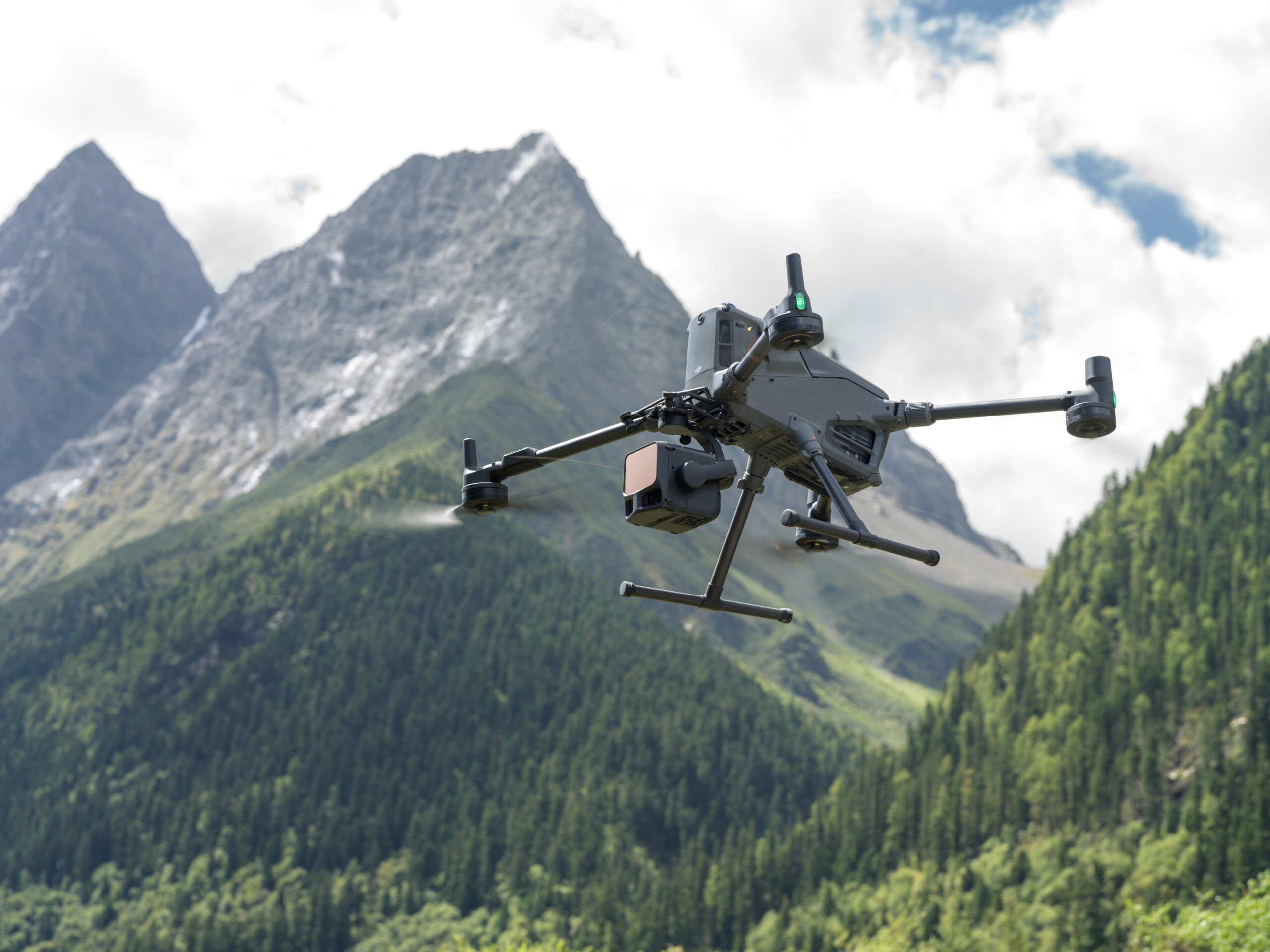 Drohne mit Zenmuse L3 LiDAR-Sensor fliegt vor bewaldeten Berghängen und Felsgipfeln