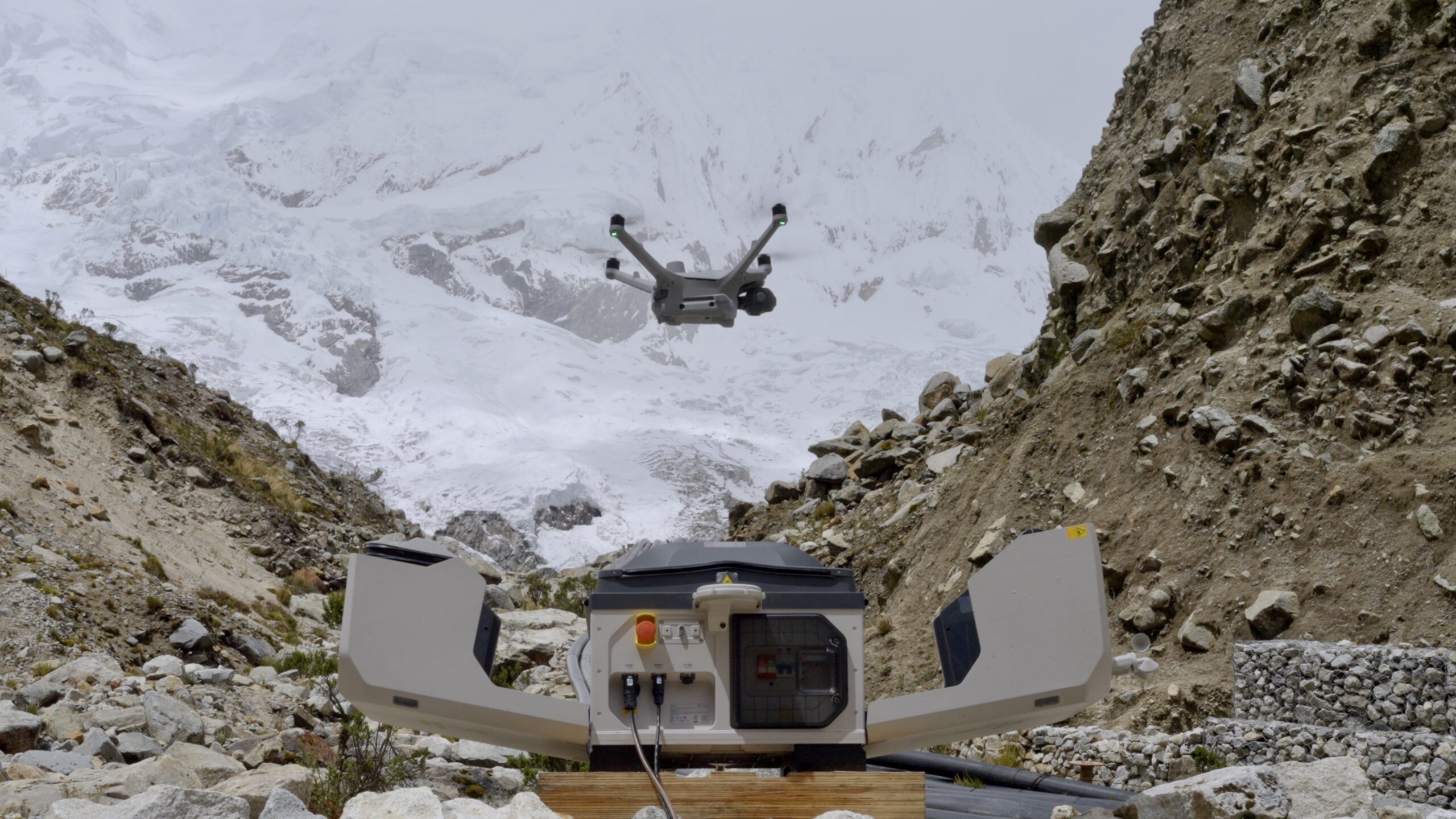 Drohne schwebt über der geöffneten DJI Dock 3 vor verschneitem Hochgebirge