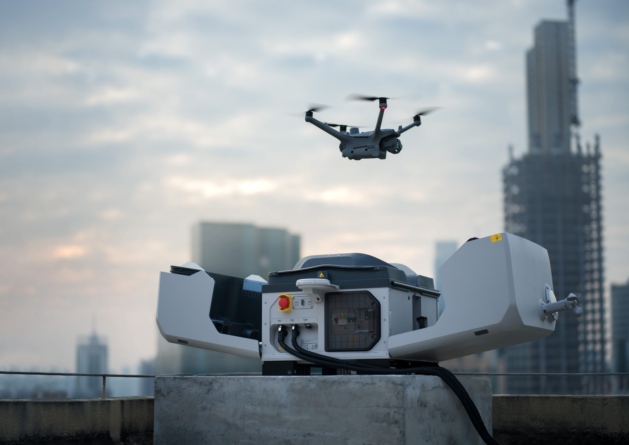Geöffnete DJI Dock 3 auf einem Hochhausdach mit Drohne im Flug vor der Stadtsilhouette