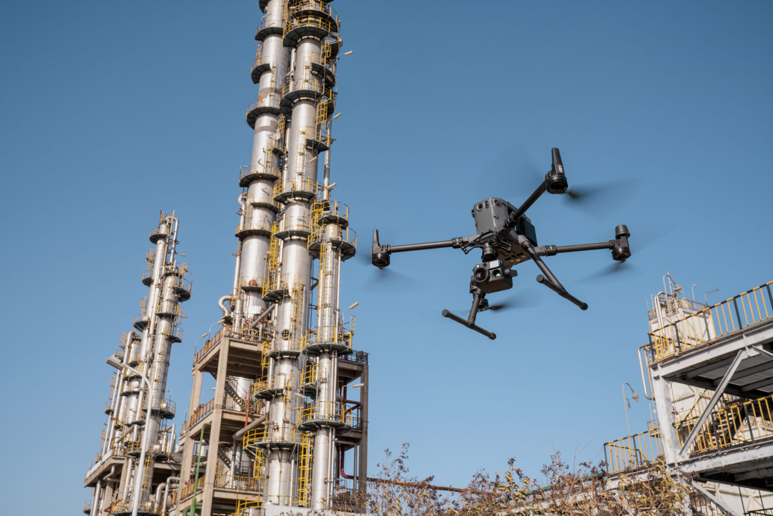 Inspektionsdrohne mit Zenmuse H30T Kamera fliegt neben den hohen Kolonnen einer Industrieanlage