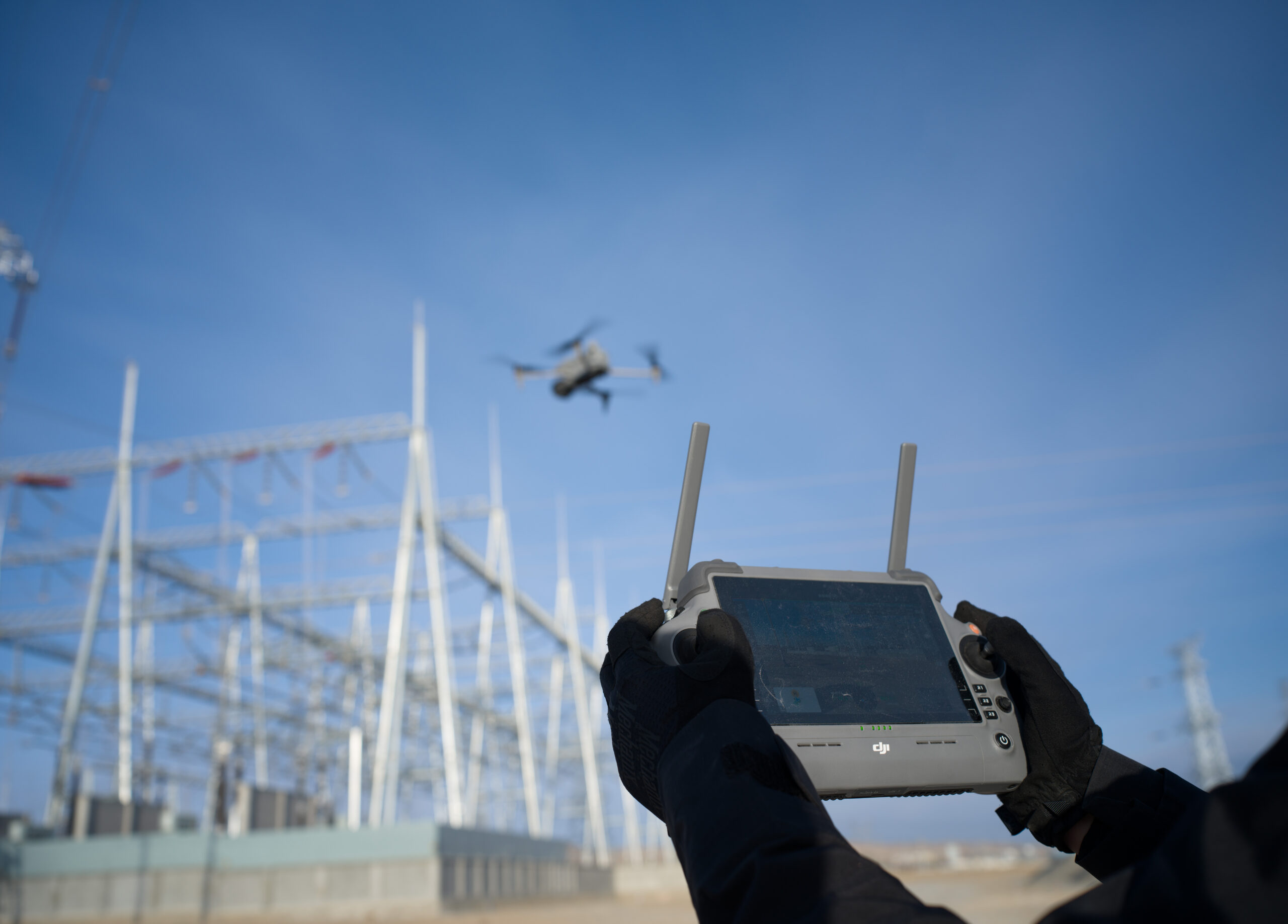 Pilot steuert mit einer DJI Fernsteuerung eine Drohne über einem Umspannwerk