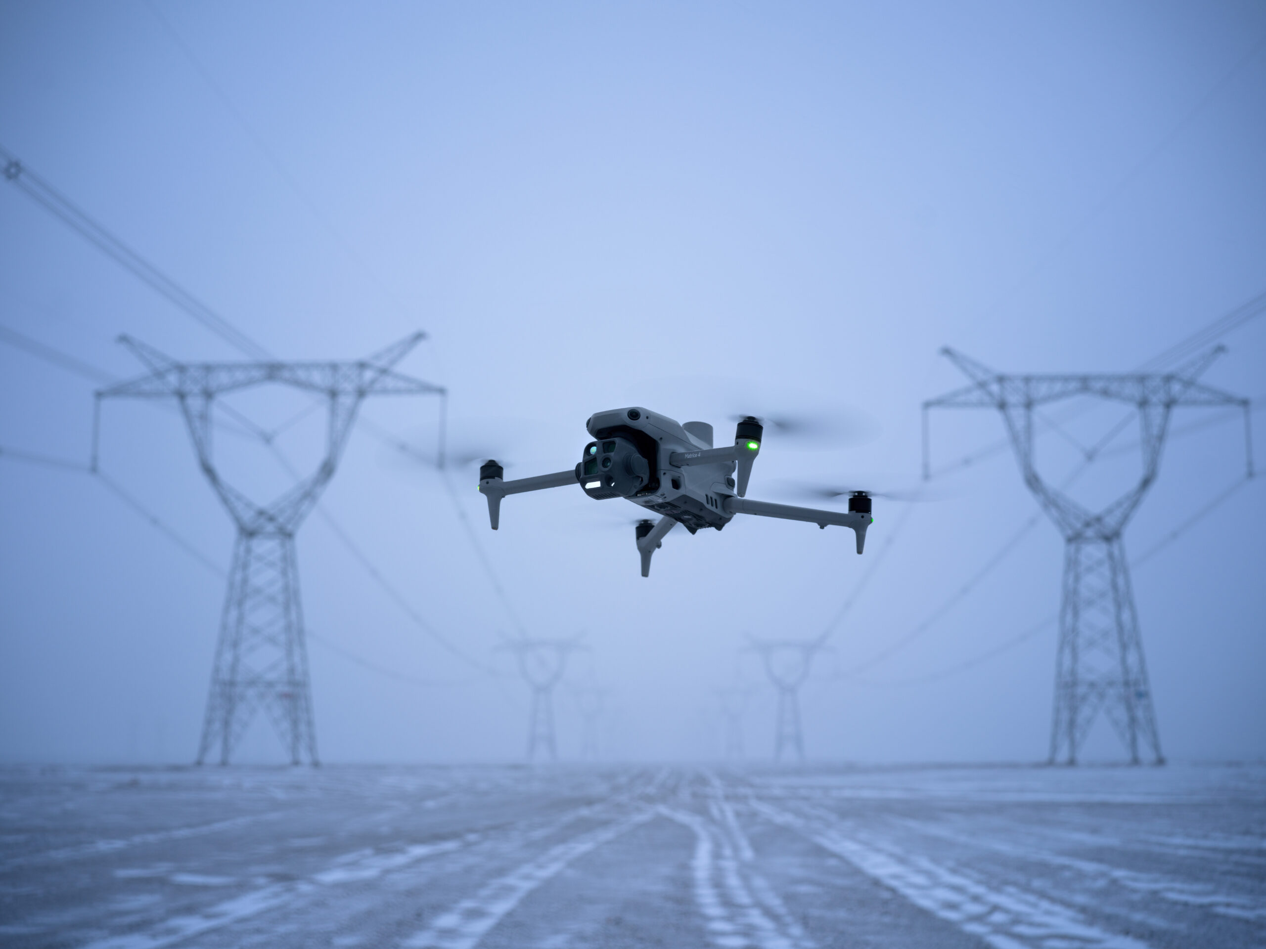 DJI Matrice 4T fliegt bei Nebel und Schnee zwischen Hochspannungsmasten