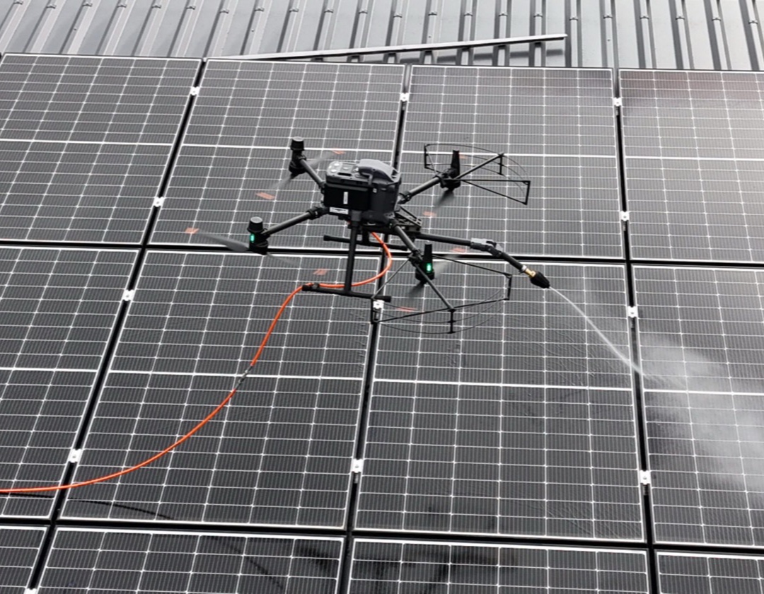 Reinigungsdrohne mit Sprühlanze reinigt Photovoltaikmodule auf einem Gebäudedach